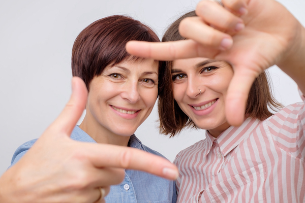 Mother and her daughter making a gesture with hands like they are making selfie and smiling